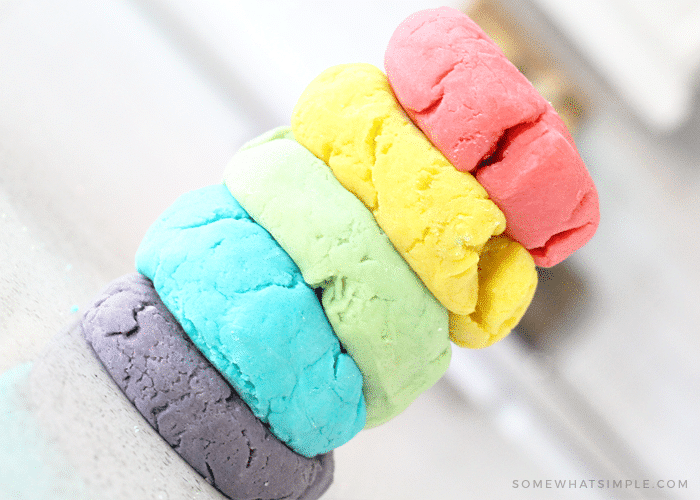 a close up picture of different colored homemade playdough stacked on top of each other and slightly flattened, made with this simple recipe