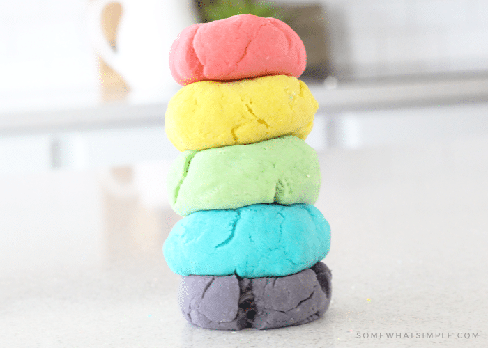 red, yellow, green, blue and purple balls of homemade playdough stacked on top of each other on a white kitchen counter