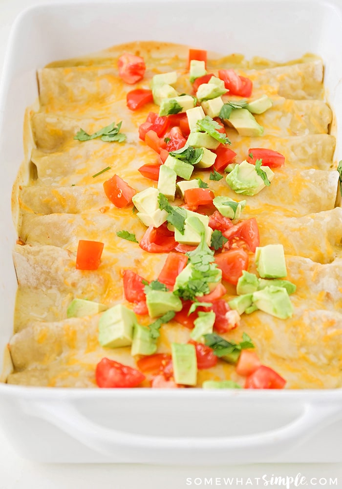 a tray of enchiladas topped with cheese, diced tomatoes and avocado