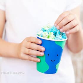 child holding a cup that looks like the earth filled with blue and green popcorn