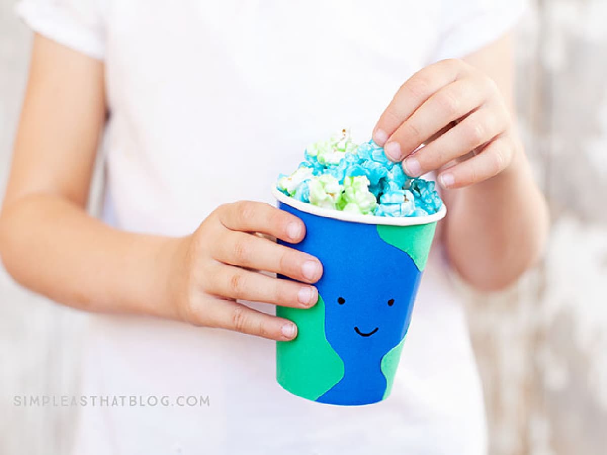 child holding a cup that looks like the earth filled with blue and green popcorn