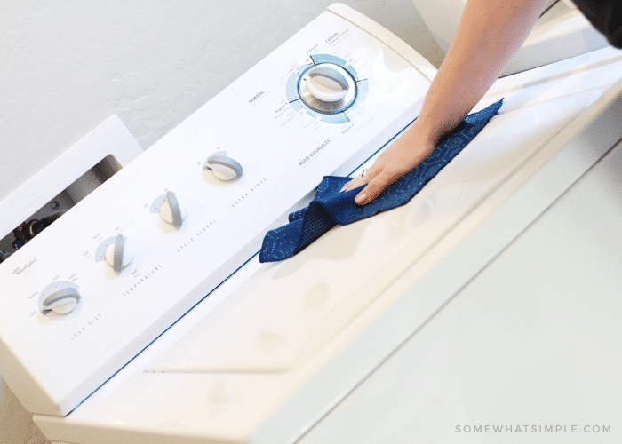 a hand wiping down the top of a top load washing machine with a blue wash cloth