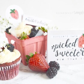 a red velvet cupcake topped with berries along with a small gift crate with another cupcake and berries sitting on the counter. Next to the gift is a Mother's Day card that reads couldn't have picked a sweeter mom than you