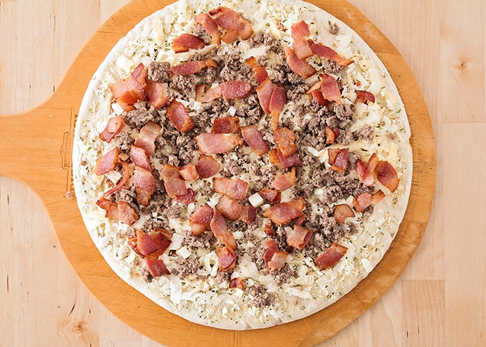 looking down on a raw pizza crust with cheese ground beef and bacon on top