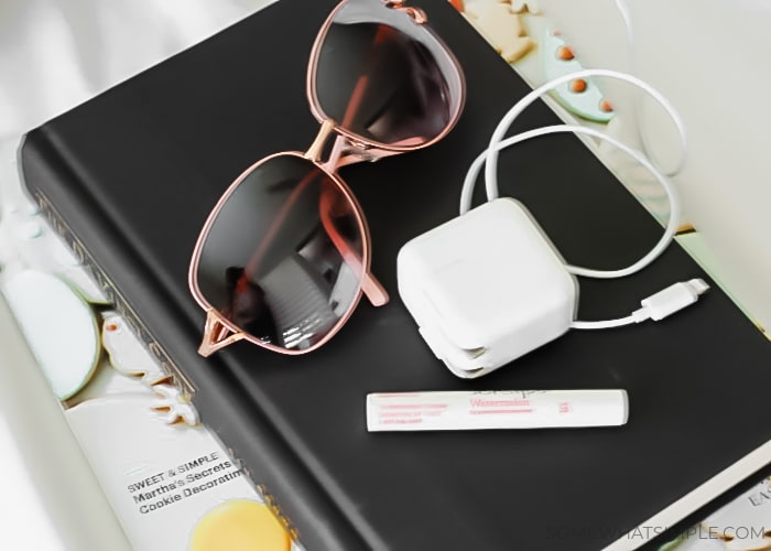 a book, a magazine, chapstick and a charger stacked next to a carry on bag
