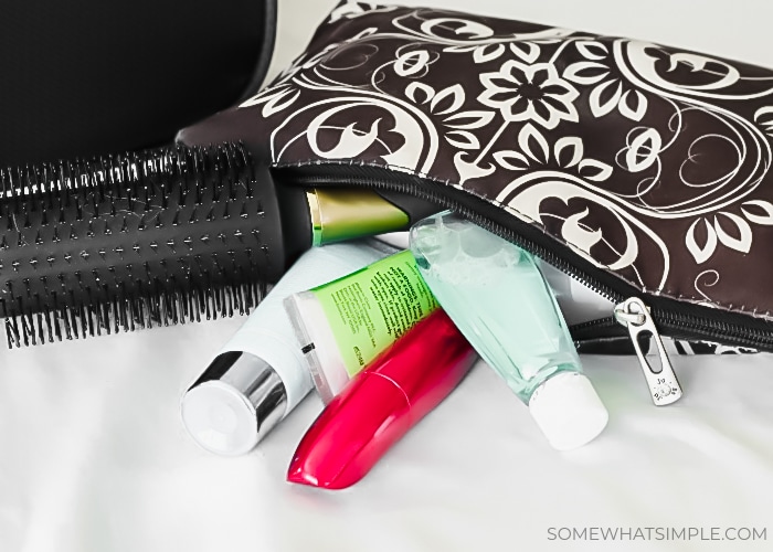 a toiletry bag with a hair brush sticking out sitting on top of a carry on suitcase