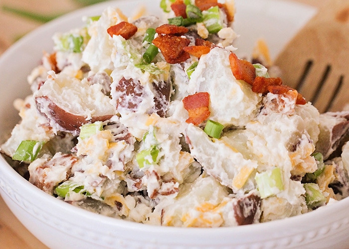 a white bowl filled with this loaded baked potato salad recipe that filled with red potatoes, bacon, cheese and green onions