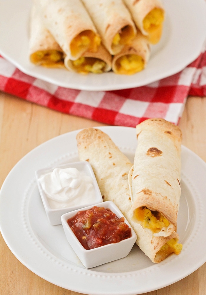 two crispy baked breakfast taquitos with a side of salsa and sour cream