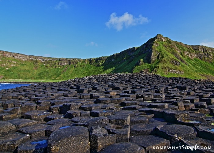 looking down a long row of the unique rock formations at the Giants Causeway with large hills in the background in Northern Ireland