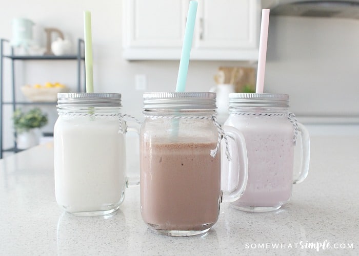 Chocolate, strawberry and vanilla Slim Fast shakes in mason jar glasses on a counter and each have a pastel colored straw