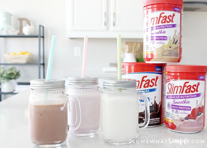 Chocolate, strawberry and vanilla Slim Fast shakes in mason jar glasses on a counter next to containers of Slim Fast smoothie mix