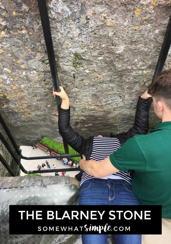 a woman laying on her back and holding on to two metal bars while she kisses the Blarney Stone at the top of the Blarney Castle in southern Ireland