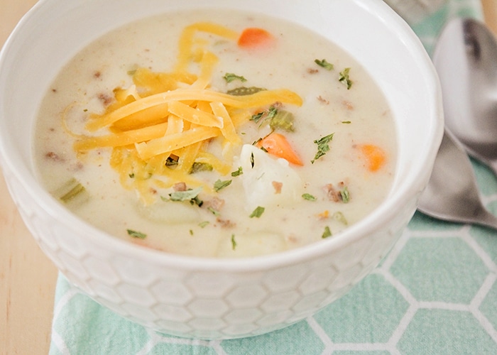 a bowl of crock pot cheeseburger soup filled with meat potatoes and vegetables, topped with shredded cheese