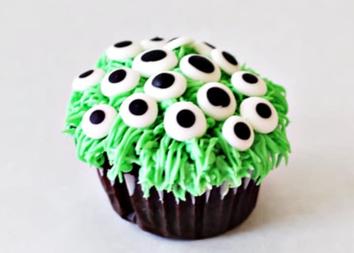 a cupcake topped with stringy green frosting and candy monster eyeballs