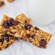 two homemade pumpkin granola bars laying on a counter top next to a glass of milk