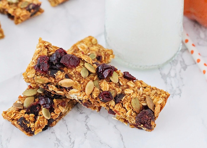 two homemade pumpkin granola bars laying on a counter top next to a glass of milk