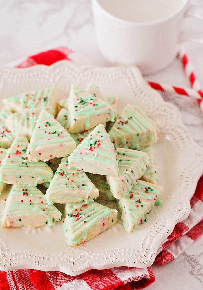 A pile of Christmas Shortbread Cookies on a white plate with red and white straws laid next to the plate.