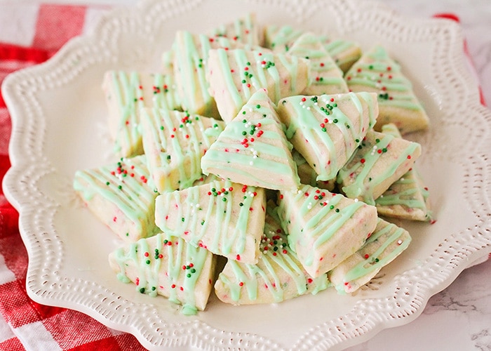 A stack of finished Shortbread Christmas Cookies on a white plate with a red and white checkered napkin under the plate.