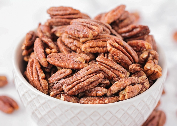 a bowl of Candied Pecans in a white bowl are a delicious super bowl treat idea