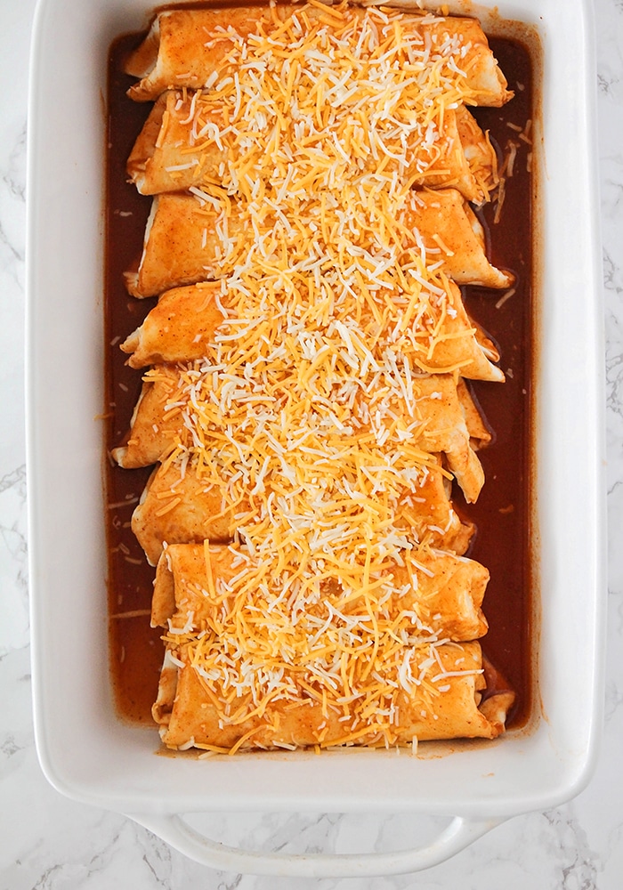 a tray with red sauce filled with enchiladas topped with cheese made using this easy chicken enchiladas recipe