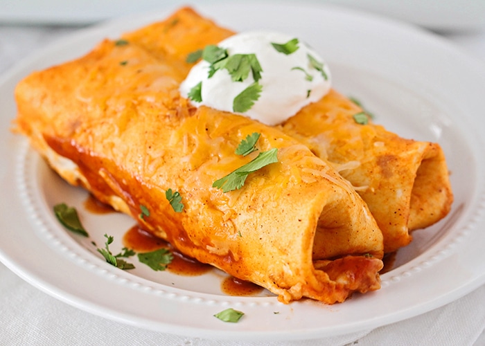 A plate with two chicken enchiladas on it topped with sour cream and parsley