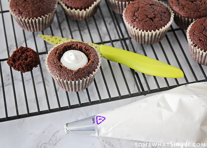 one of the chocolate cupcakes on the cooling rack has the top cut out and is filled white cupcake filling for these Homemade Hostess Cupcakes