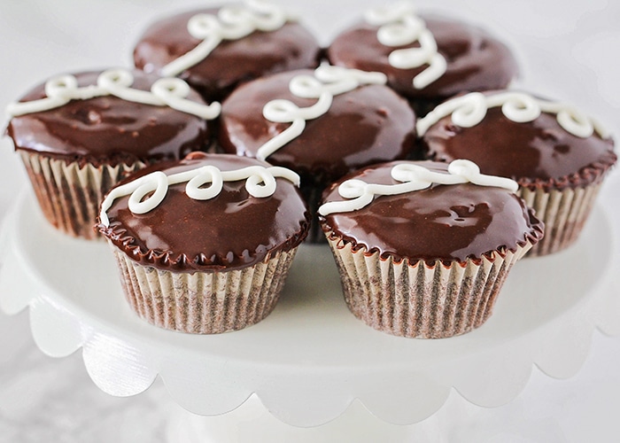 a white cupcake stand full of Homemade Hostess Cupcakes made using this recipe with chocolate icing and a swirl of the cream filling on top