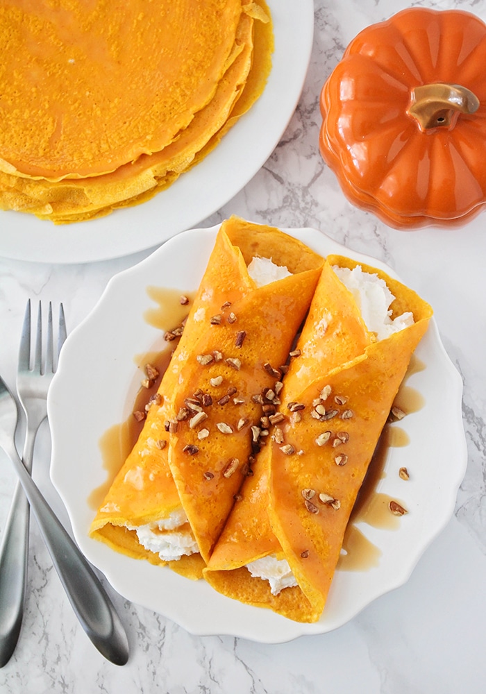 looking down on a pair of savory homemade Pumpkin Crepes with a creamy filling and a stack of cooked crepes behind them