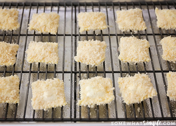several prebaked toasted raviolis placed on cooling racks on top of baking sheets before they are placed in the oven