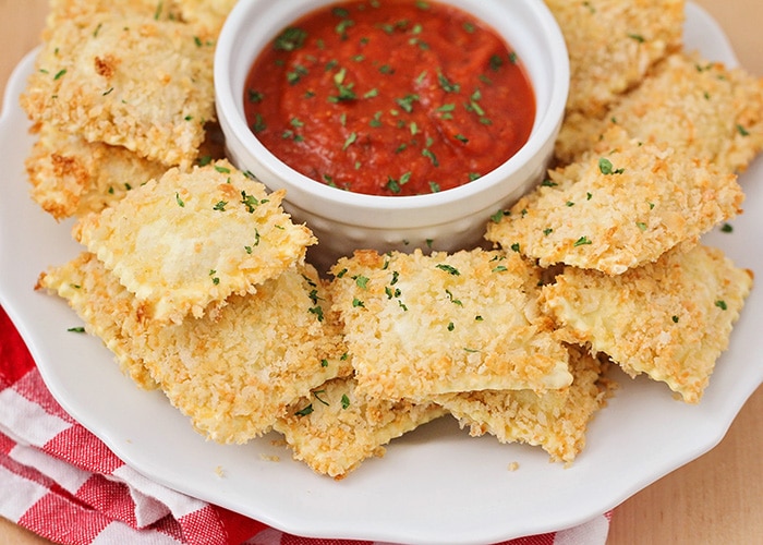 a pile of Toasted Ravioli on a plate with a marinara dip in the middle is a super bowl fan favorite