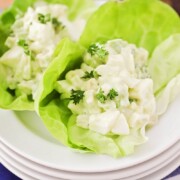 looking down on a stack of white plates with two large leaves of lettuce on top with each filled with a serving of Avocado Egg Salad