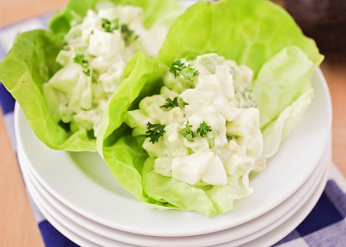 looking down on a stack of white plates with two large leaves of lettuce on top with each filled with a serving of Avocado Egg Salad