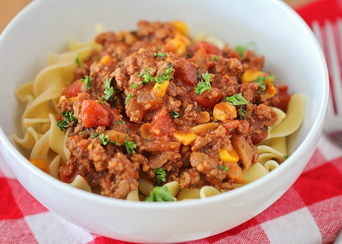 a bowl of Homemade American Goulash in a white bowl that's sitting on top of a red checkered napkin