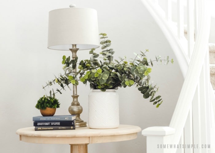 a circular natural wood table with a plant, lamp and books on top.