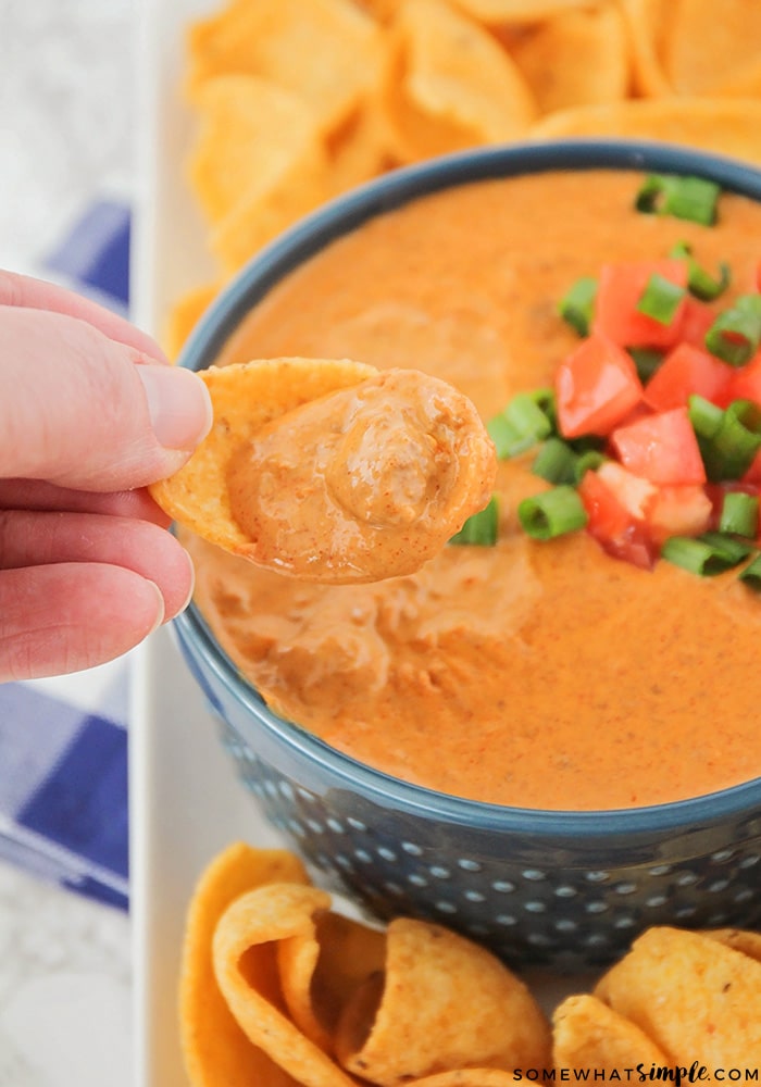 A Frito corn chip being dipped into this eas Chili Cream Cheese Dip recipe. The chili dip is topped with green onions and diced onions