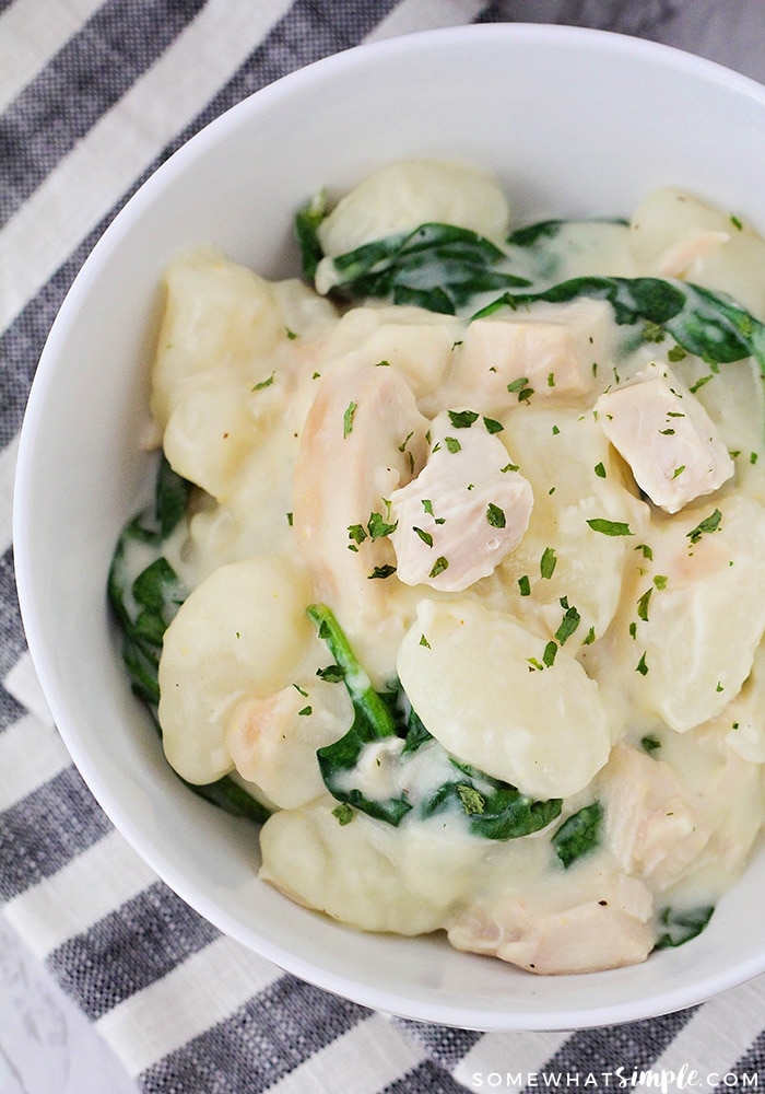 a bowl of gnocchi with chunks of chicken and spinach