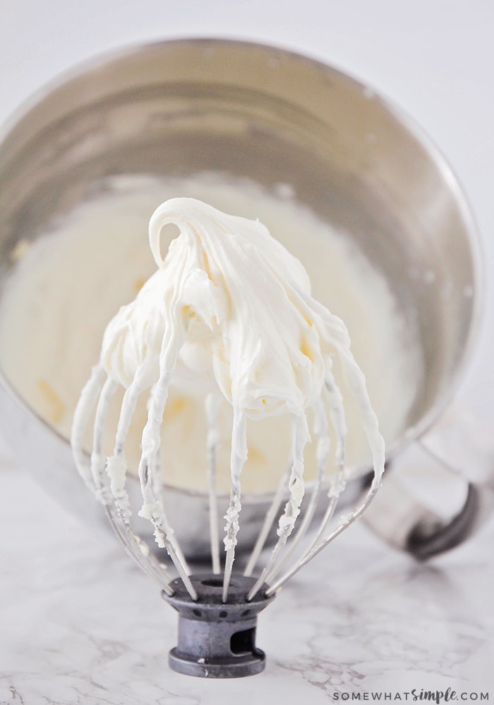 wire whip mixer attachment covered in this easy cream cheese frosting with a mixing bowl behind it filled with this homemade cream cheese frosting