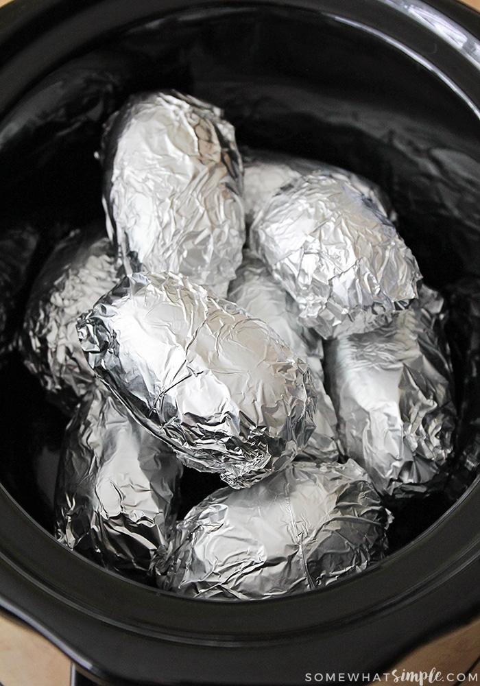 several potatoes wrapped in aluminum foil and placed in a crock pot