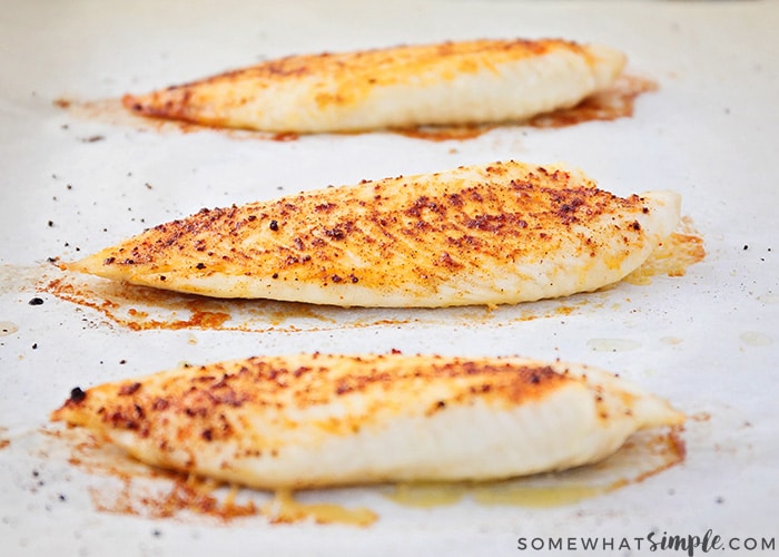 three baked and seasoned tilapia fillets on a baking sheet ready to be included in this easy fish taco recipe