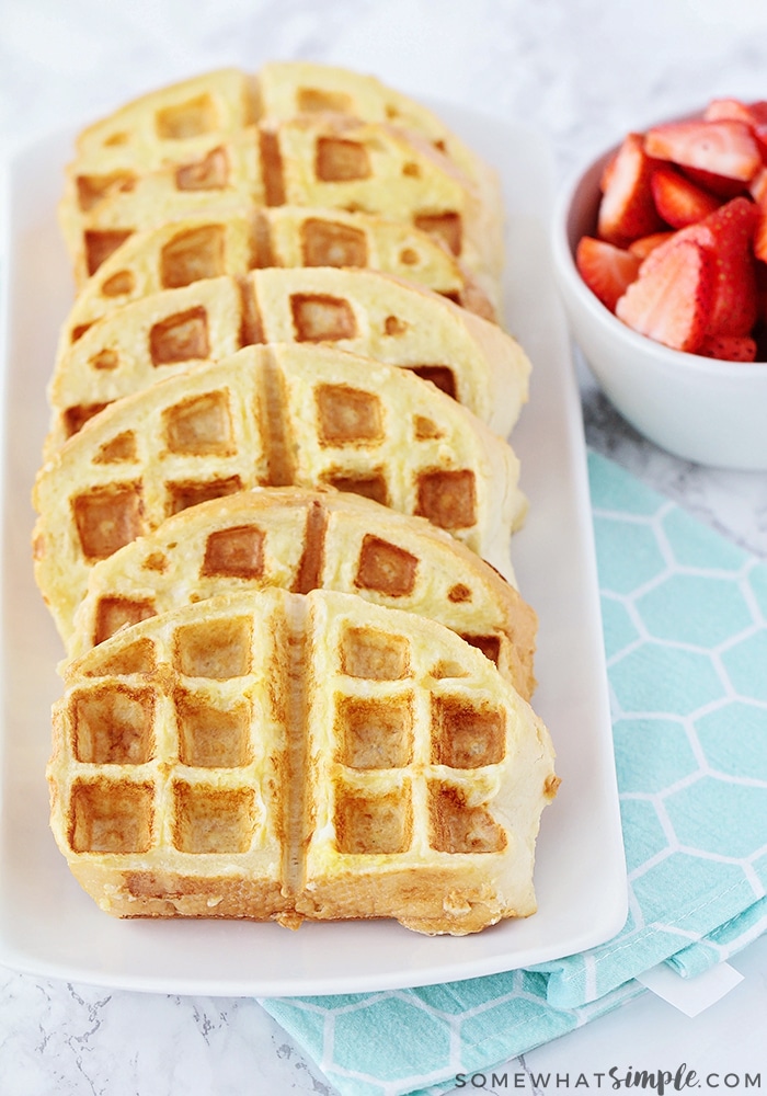 looking down on a white tray of seven of the Best French toast waffles with a bowl of sliced strawberries next to them