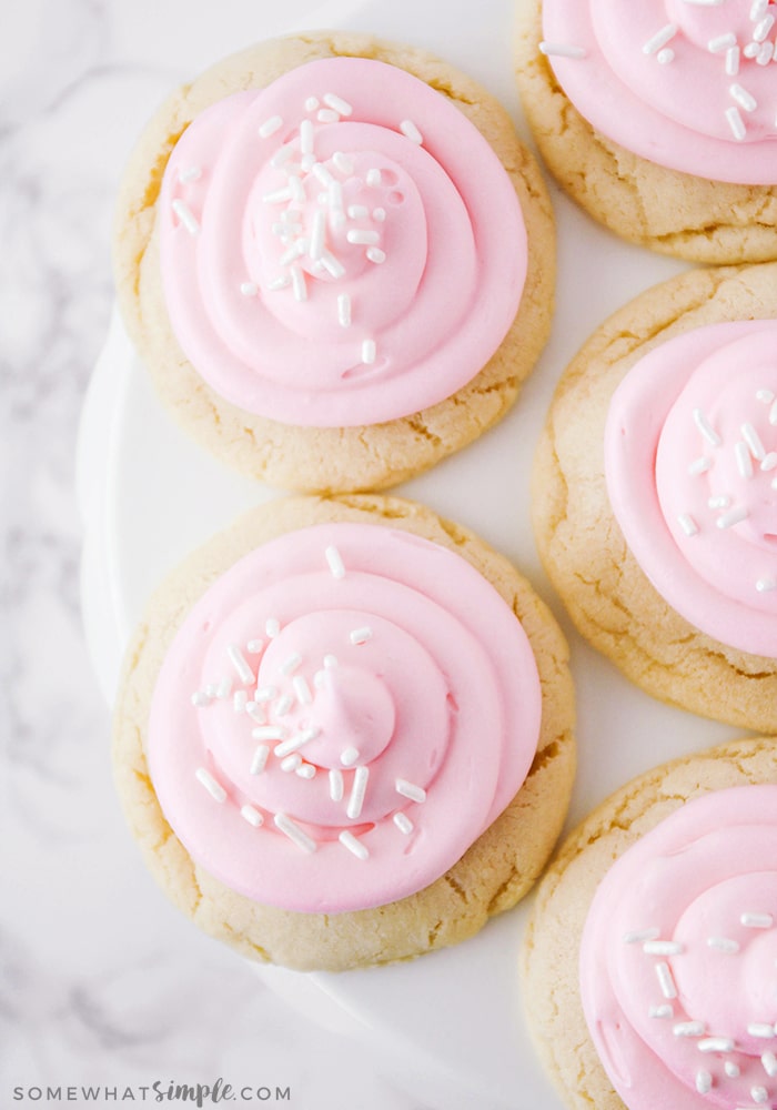 looking down on a serving tray filled with sugar cookies, topped with pink frosting and white sprinkles, made with this easy 10 minute recipe
