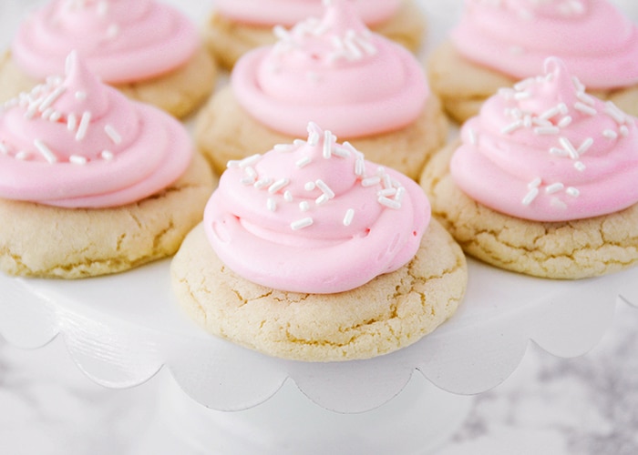 a serving tray filled with easy sugar cookies topped with pink frosting and white sprinkles