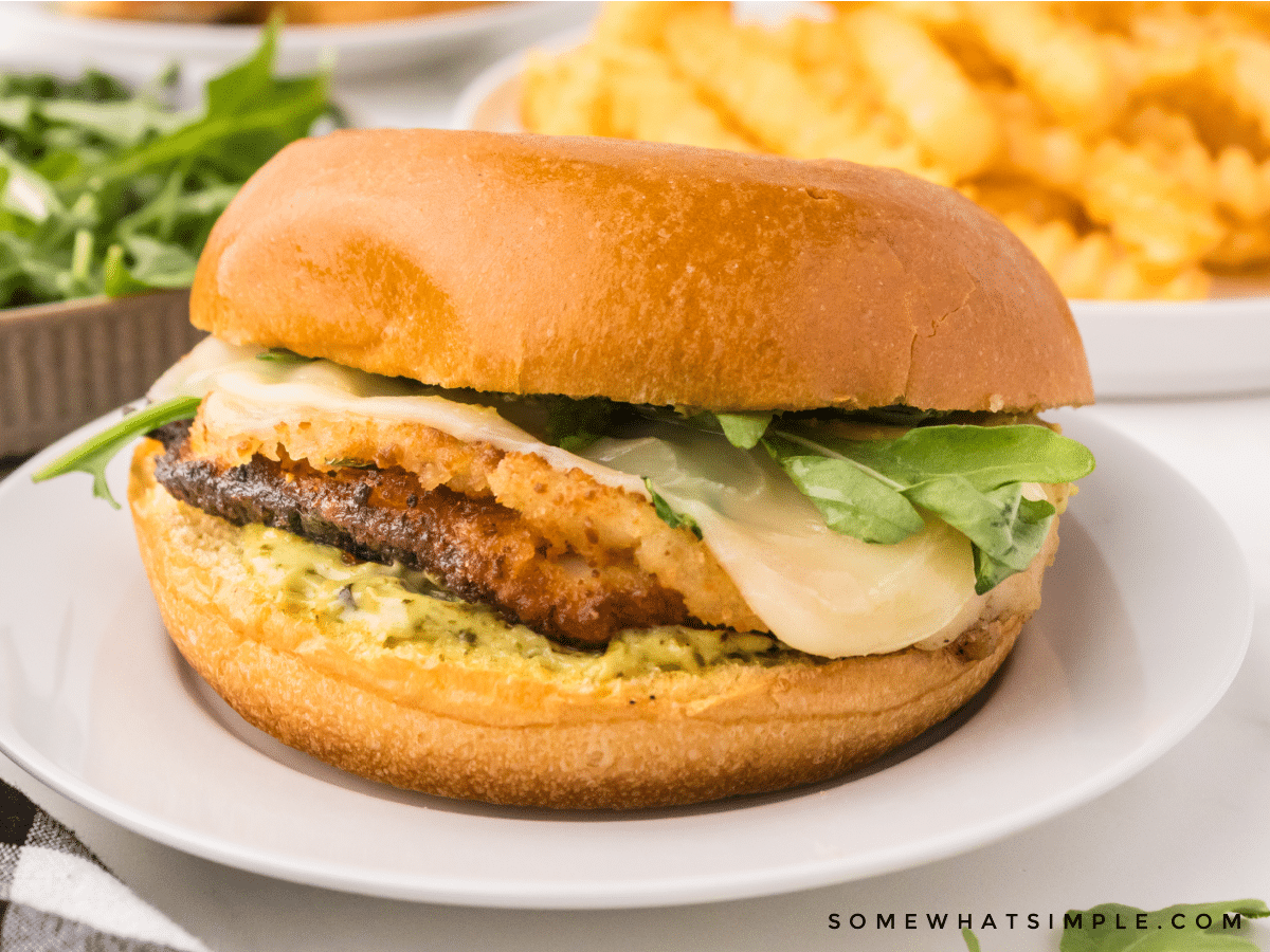 plated chicken sandwich on a white plate with french fries in the background