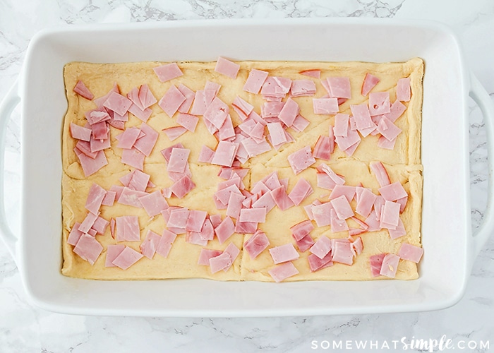 a white casserole pan with Pillsbury croissant dough lining the bottom with diced pieces of ham sprinkled over it