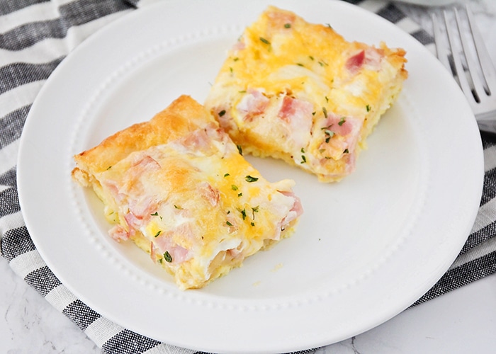 two squares of a croissant breakfast egg casserole made with ham on a white plate sitting on top of a cloth black and white striped napkin.