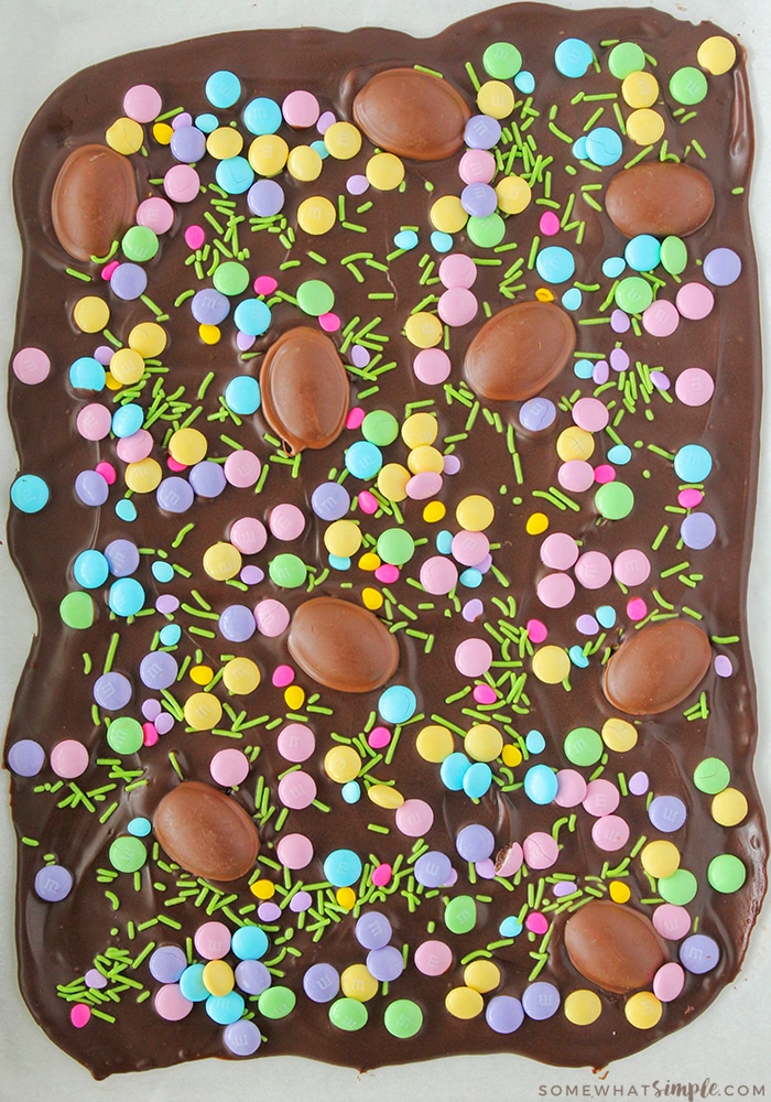 looking down on a cookie sheet filled with dark chocolate and pastel colored candy and chocolate eggs sprinkled over it