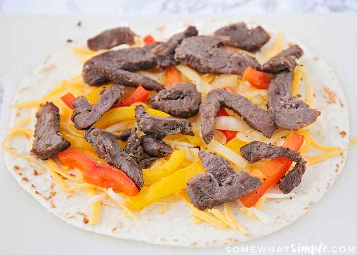 a tortilla topped with shredded cheese, steak, onions and bell peppers