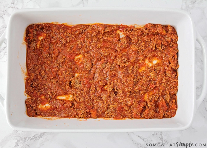 a casserole dish with a layer of homemade meat sauce on the bottom