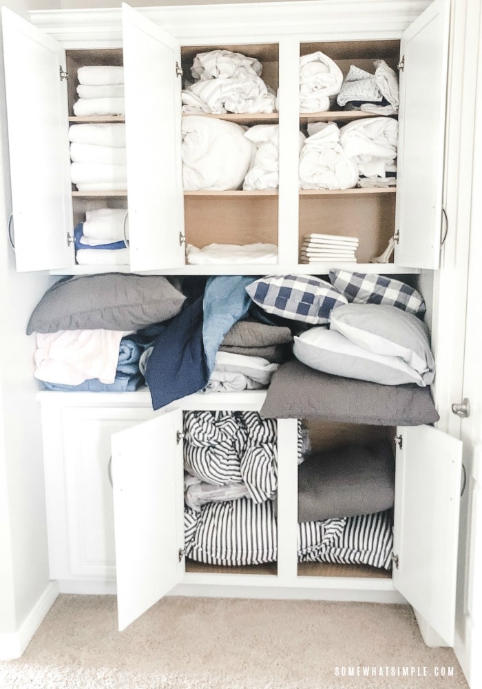 all of the doors of a linen closet are open revealing a mess of towels, pillows and sheets that are stuffed inside and completely unorganized.