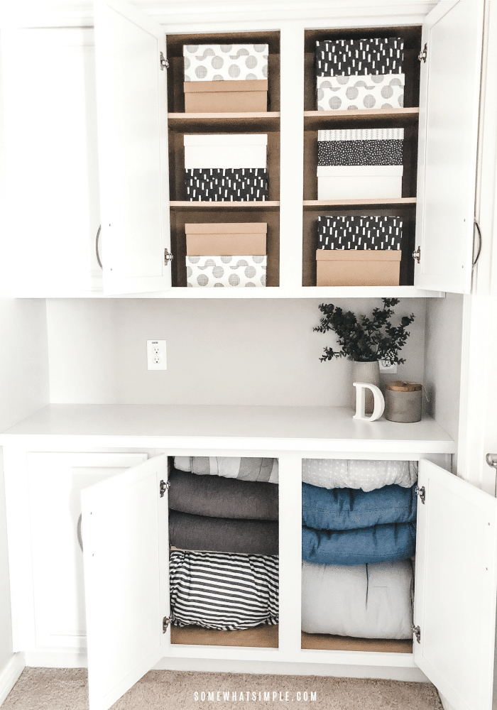 the doors of an organized white linen closet that are open revealing neatly stacked boxes and folded blankets